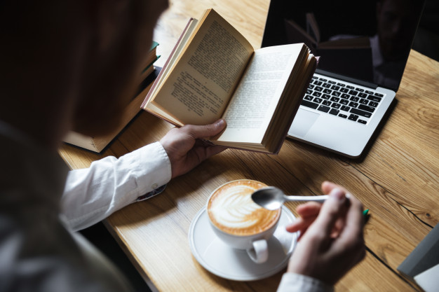 top-view-man-white-shirt-stirring-coffee-while-reading-book_171337-10016